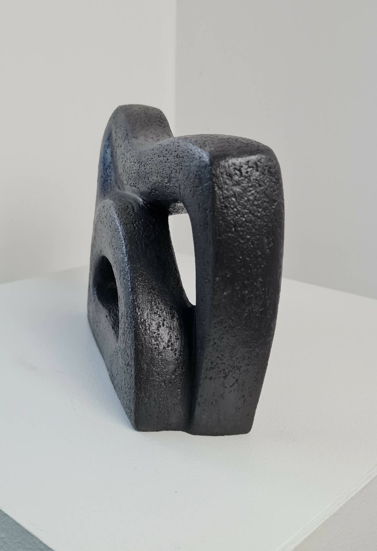 Sculpture abstraite sombre en angle, relief granuleux et ouvertures asymétriques.