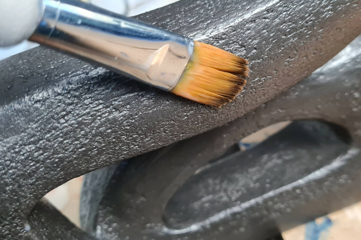 Application de peinture sur sculpture abstraite sombre : pinceau sur surface granuleuse.