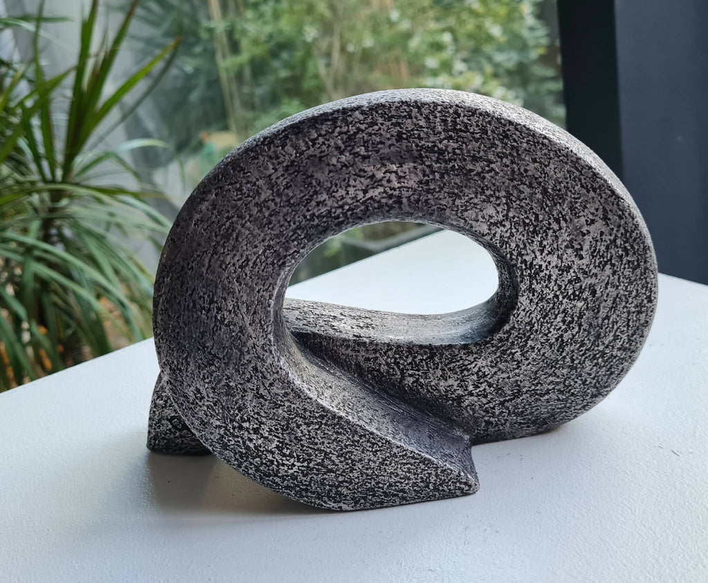 Sculpture abstraite en pierre sombre, boucle ovale posée sur une surface