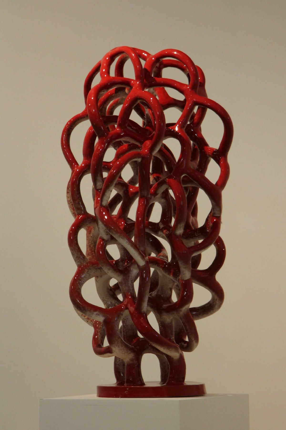 Sculpture décorative abstraite en nœuds de métal rouge sur socle blanc.