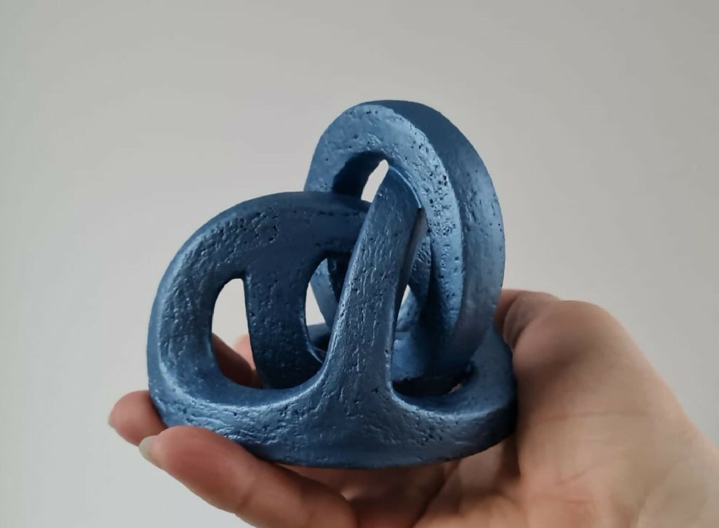 Sculpture abstraite bleue tenue à la main, anneaux ajourés sur socle.
