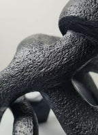 Détail de sculpture sombre à texture granuleuse, courbes avec ouvertures