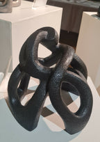 Sculpture abstraite sombre posée sur socle, vue en diagonale