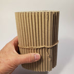 Tube en carton ondulé beige tenu par la main, ficelle autour