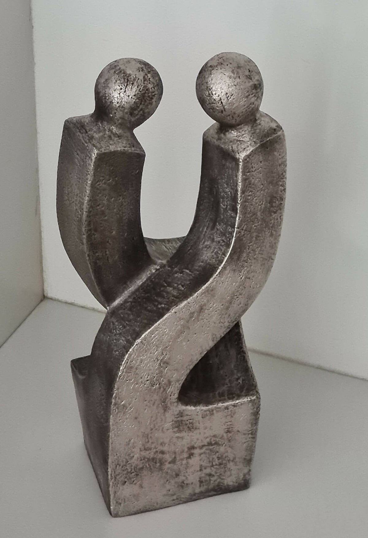 Sculpture de couple en métal gris patiné, vue en angle avec silhouettes appuyées
