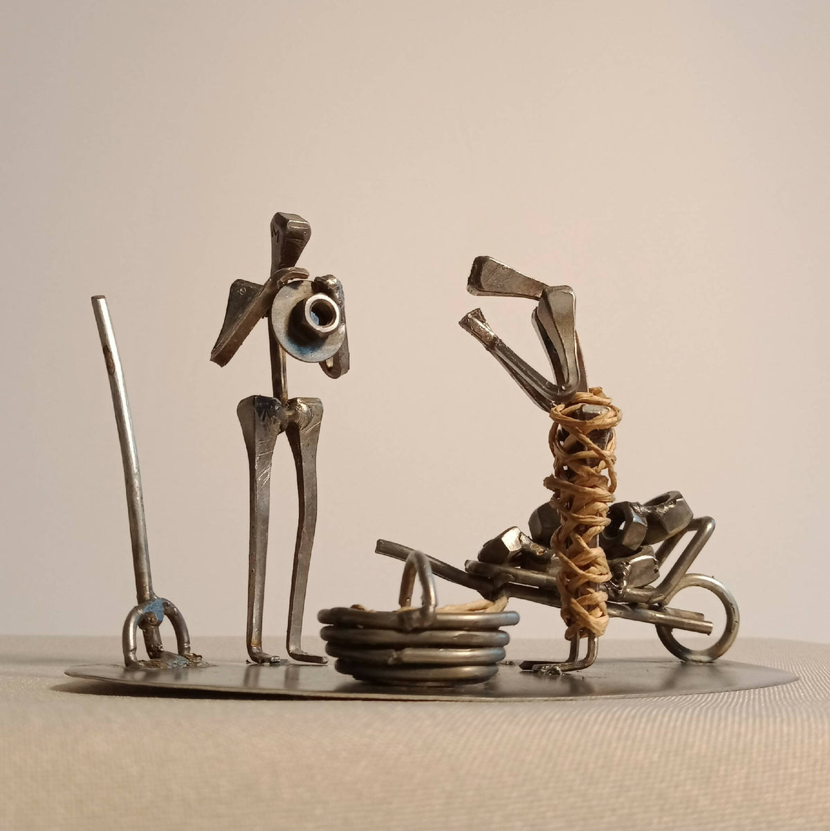 Sculpture décorative en métal, deux personnages mécaniques sur socle circulaire.