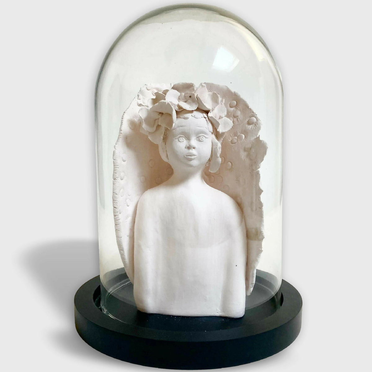 Sculpture d'enfant blanche avec fleurs en relief, sur base noire.