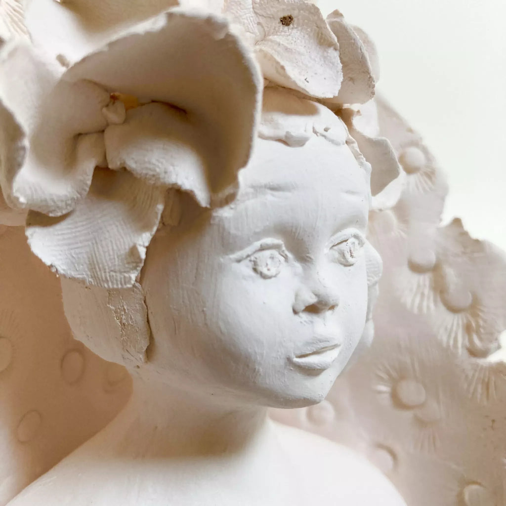 Profil d'enfant sculpté blanc, fleurs en relief et textures gravées.