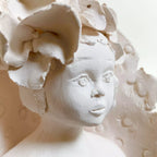 Profil d'enfant sculpté blanc, fleurs en relief et textures gravées.