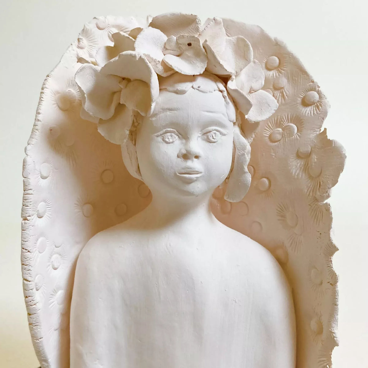 Sculpture d'enfant blanche en buste, fleurs en relief sur la tête.