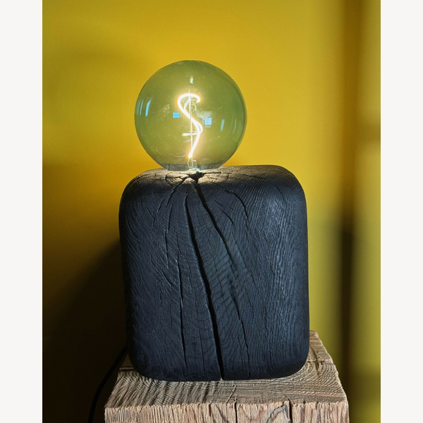 Sculpture lumineuse à ampoule sphérique vert émeraude sur base cubique bleu foncé.