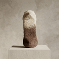 Sculpture cylindrique granuleuse, haut beige clair, bas brun foncé, posée sur socle.