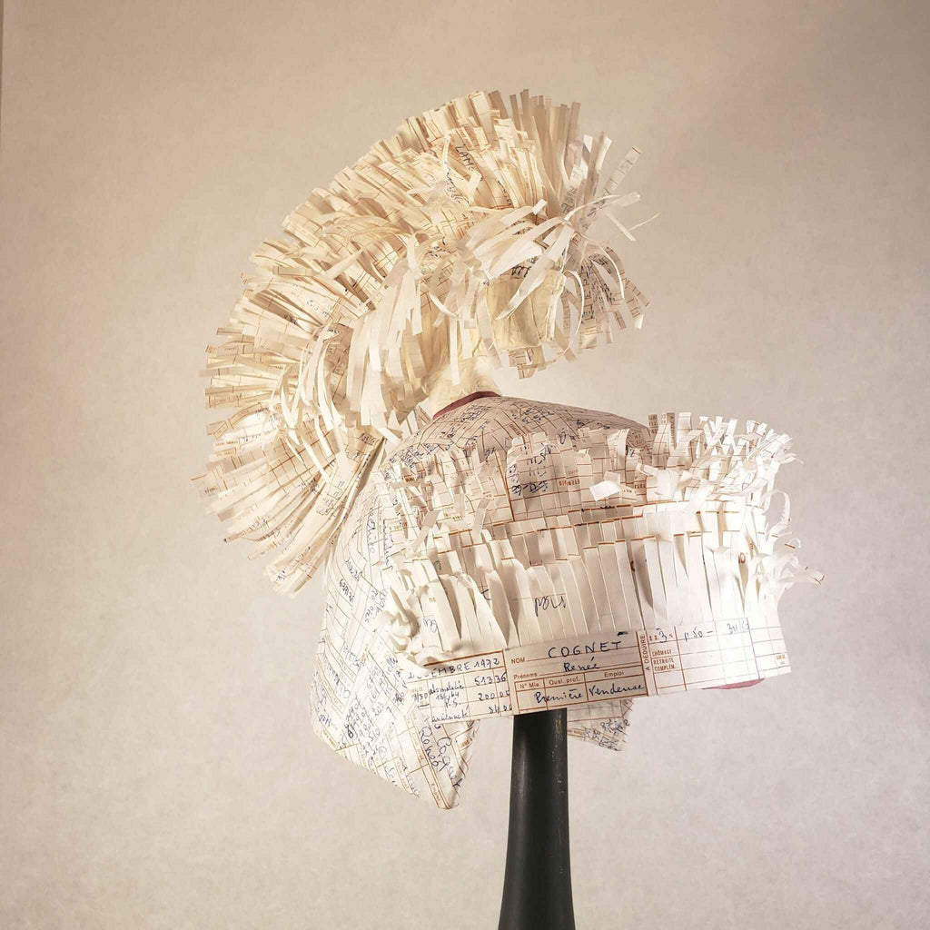 Casque à aigrette en papier froissé beige, monté sur base noire, vue de trois-quarts.