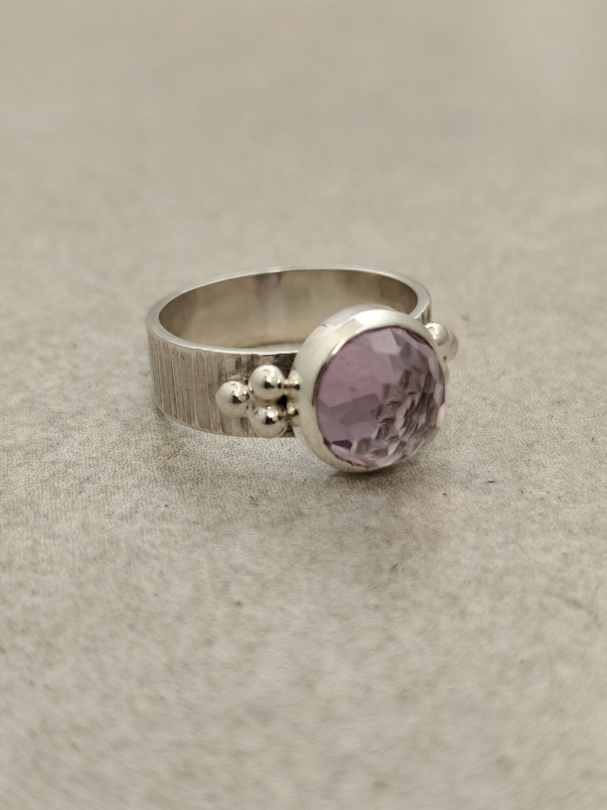 Bague argentée large à pierre améthyste ronde, monture latérale avec billes.