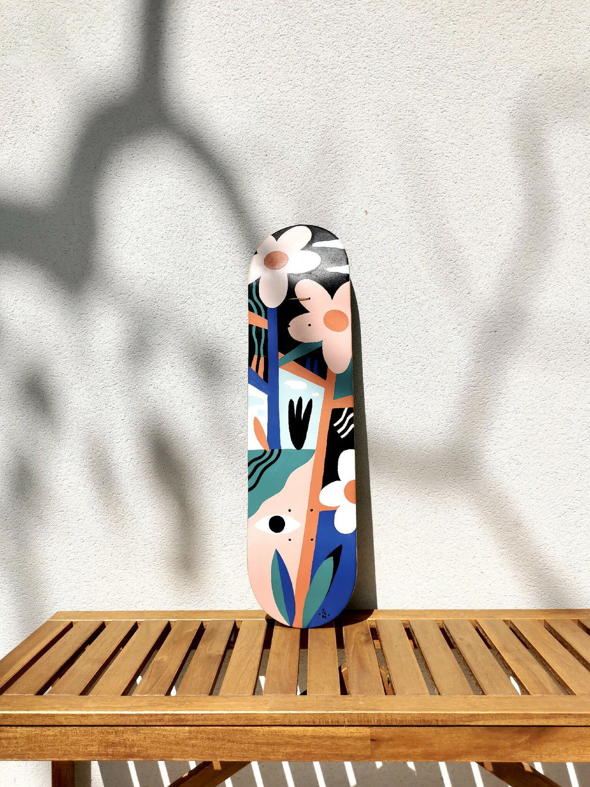 Skateboard vertical, illustré de visages stylisés et fleurs, motifs bleu, orange et noir.