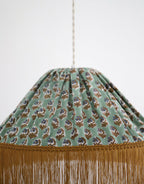 Détail de la suspension : tissu vert à motif floral et franges dorées sur la bordure.