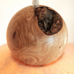 Sphère en bois veiné avec ouverture en feutre noir moucheté autour de l’ampoule.