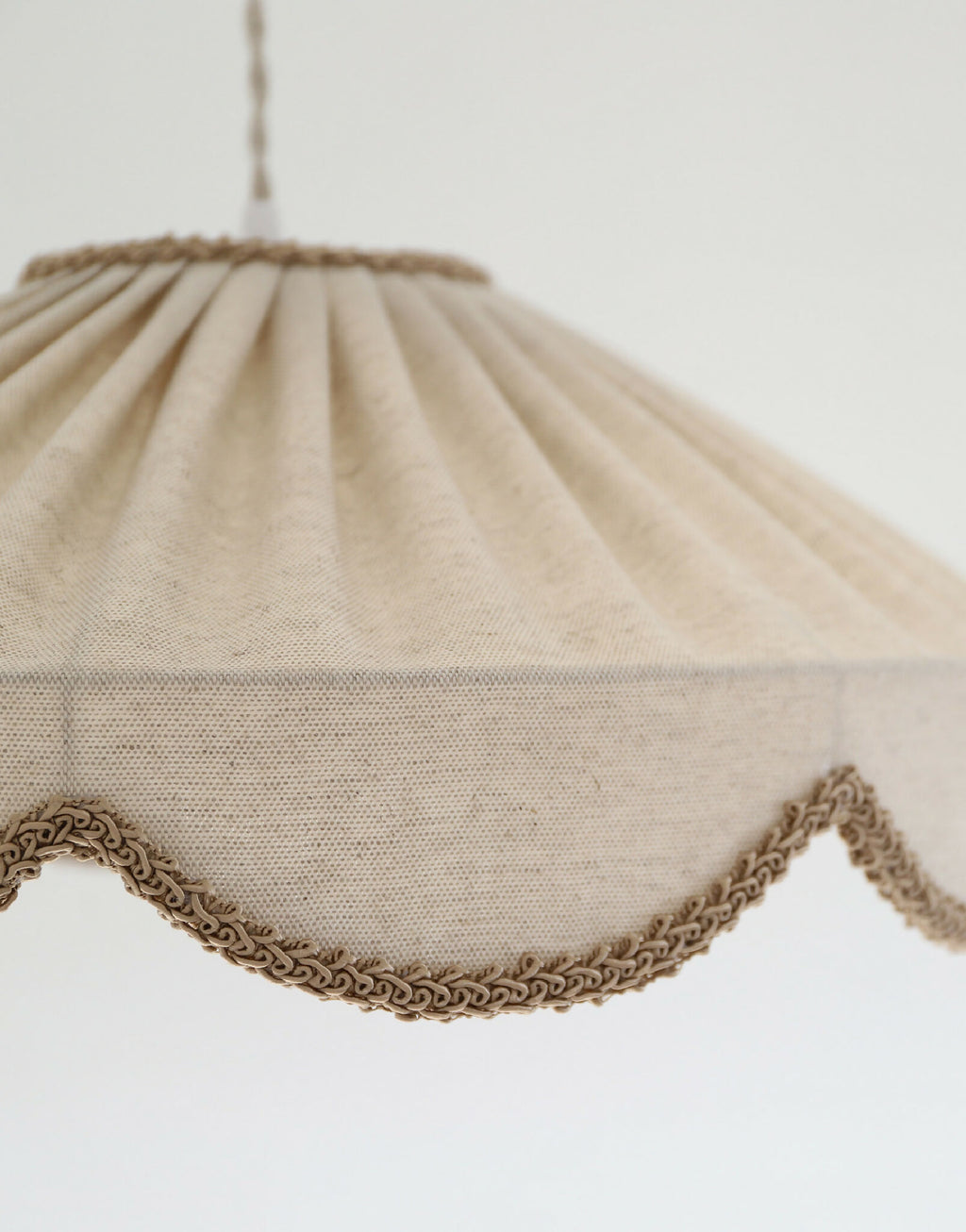Abat-jour suspendu en tissu beige, détail de bordure festonnée en tresse