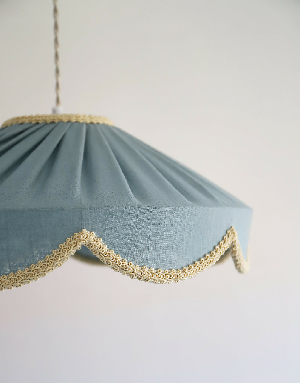 Suspension en tissu bleu minéral, gros plan sur liseré doré ondulé sur le bord