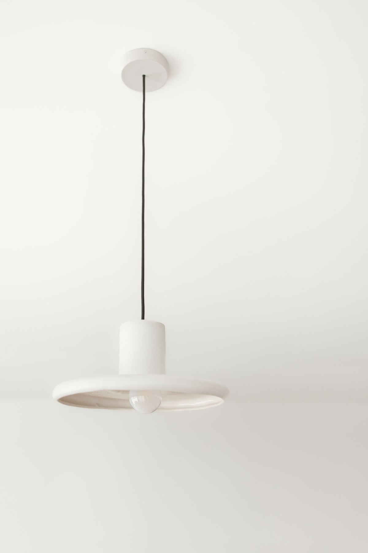 Suspension blanche mate, abat-jour disque et boîtier cylindrique au plafond, câble noir.