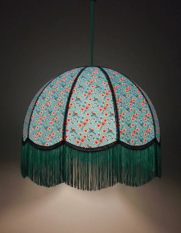Suspension en papier bleu à motifs fleuris, franges vertes et liséré noir.