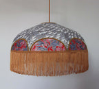 Suspension rétro : abat-jour rond gris à motifs japonais et franges dorées en bordure.