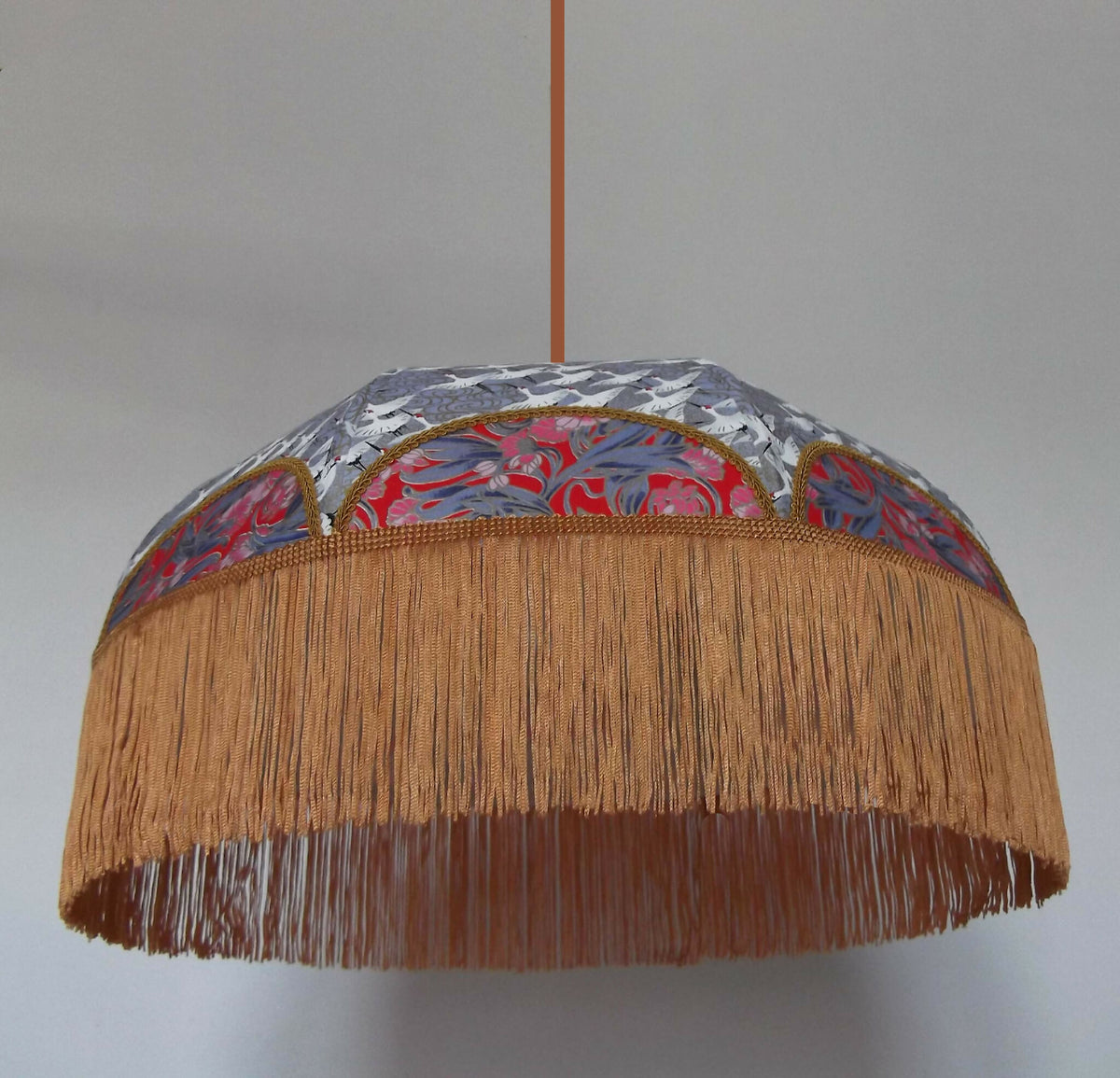 Suspension rétro : abat-jour rond gris à motifs, intérieur rouge et franges dorées.
