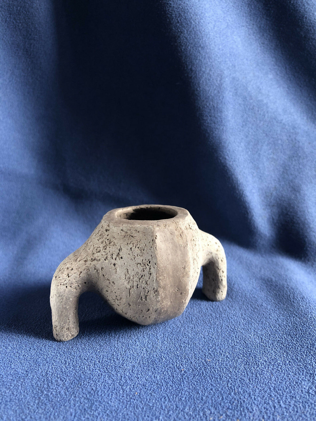 Petit pot en pierre gris clair, forme irrégulière, deux supports latéraux, ouverture.