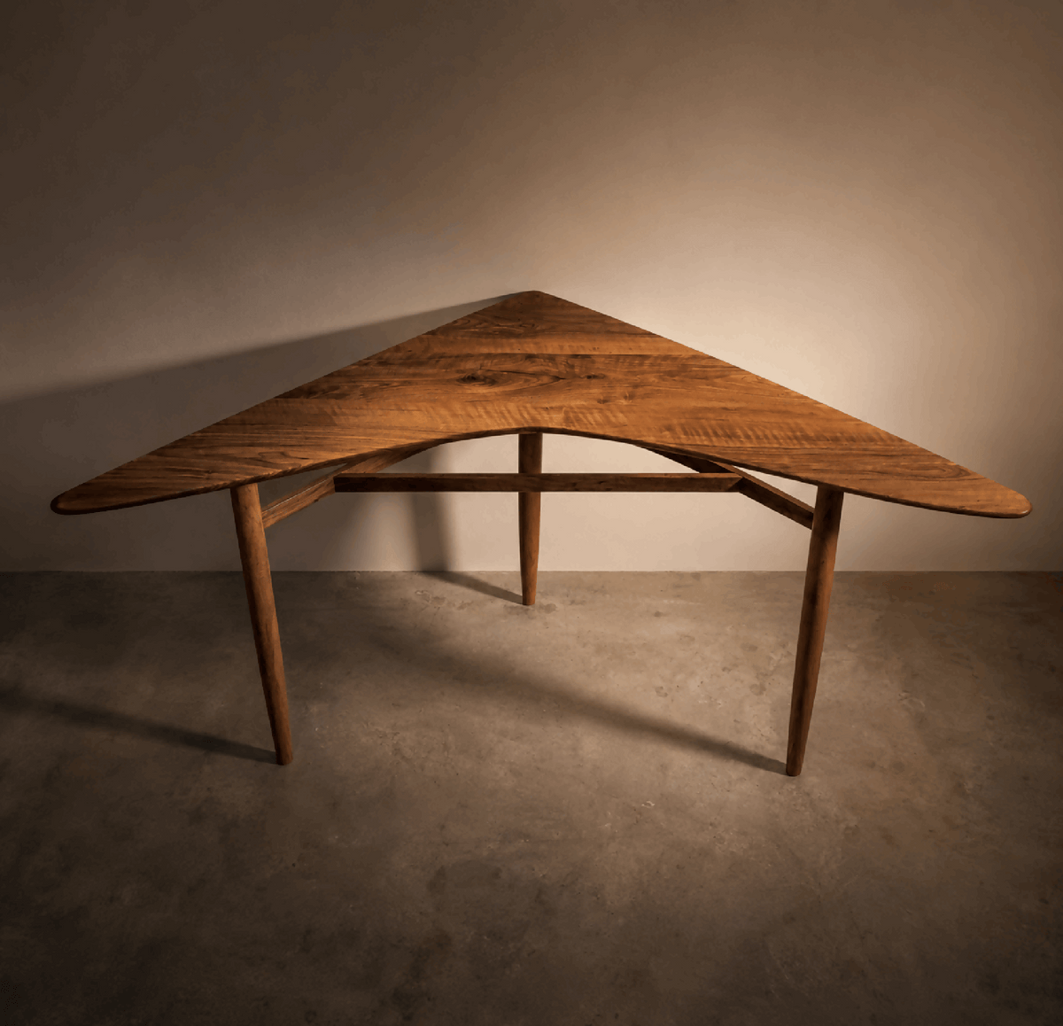 Table d’angle en bois brun, plateau cintré, structure en barreaux sous le plateau.