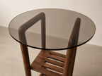 Table d’appoint ronde, plateau en verre fumé et structure en bois avec étagère à lattes.