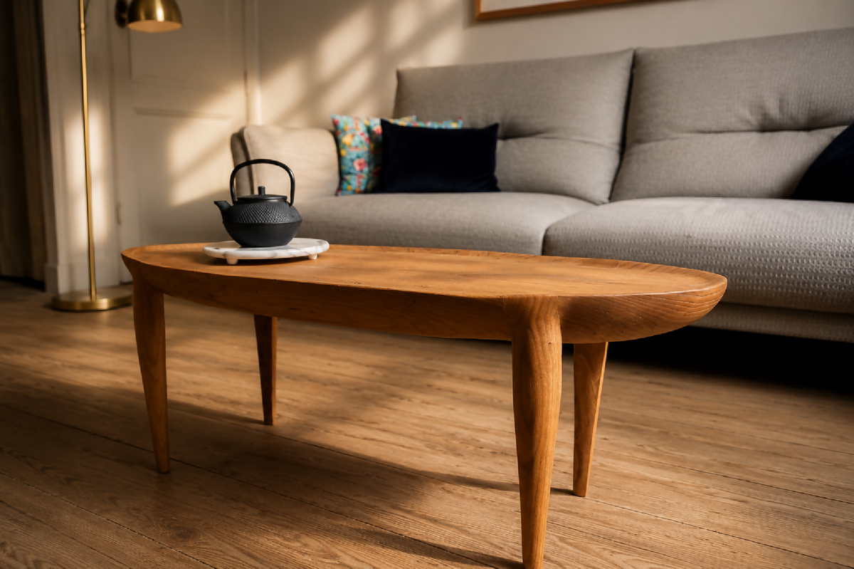 Table basse ovale en bois, pieds évasés, plateau avec bouilloire noire.