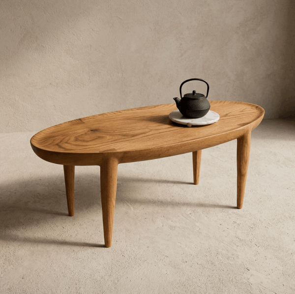 Table basse en bois au plateau ovale, pieds galbés, avec bouilloire sur un dessous de tasse.