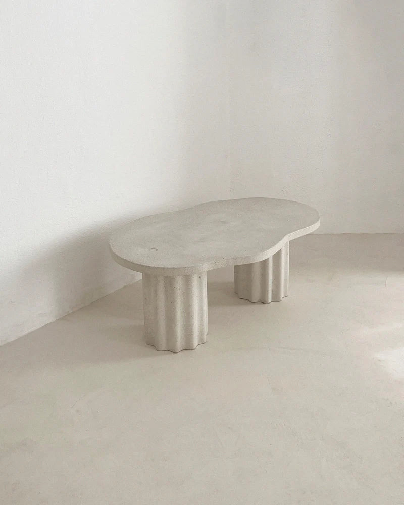 Table basse HESTIA ovale, plateau clair et pieds cylindriques cannelés visibles.
