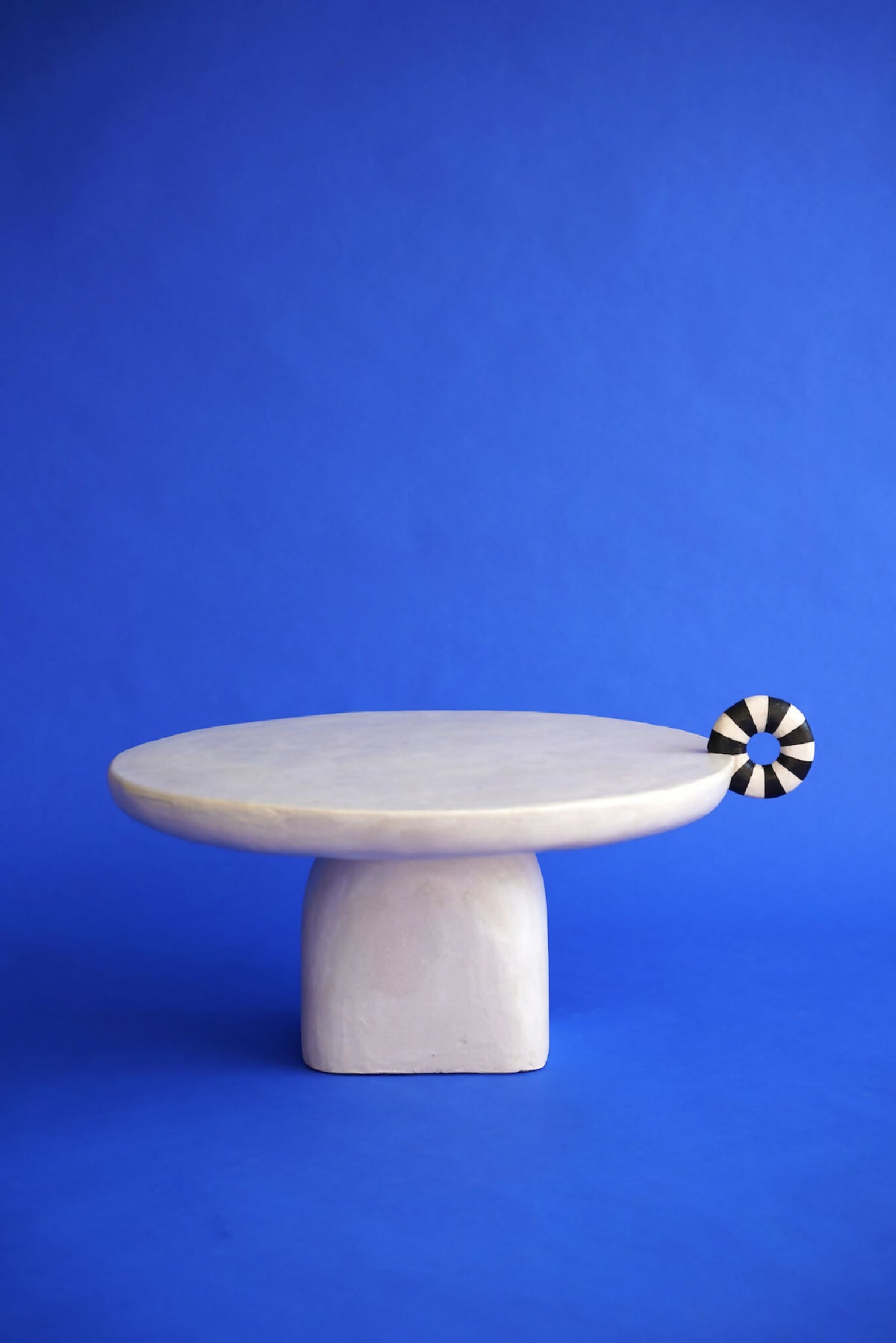 Table sculpture blanche, plateau ovale vu de côté, base cylindrique, disque décor noir&blanc