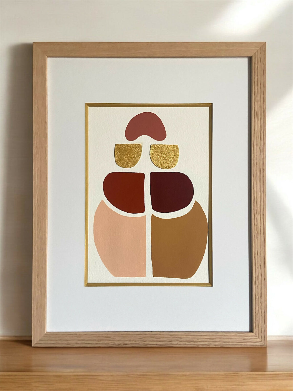 Tableau encadré en bois, composition symétrique de formes superposées en rouge et ocre.