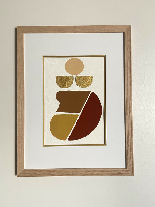 Tableau abstrait encadré en bois clair, motifs géométriques dorés et rouges sur fond clair.