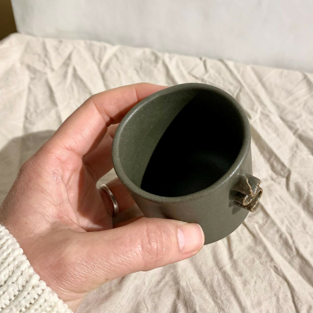 Tasse à café vert foncé avec intérieur sombre visible.