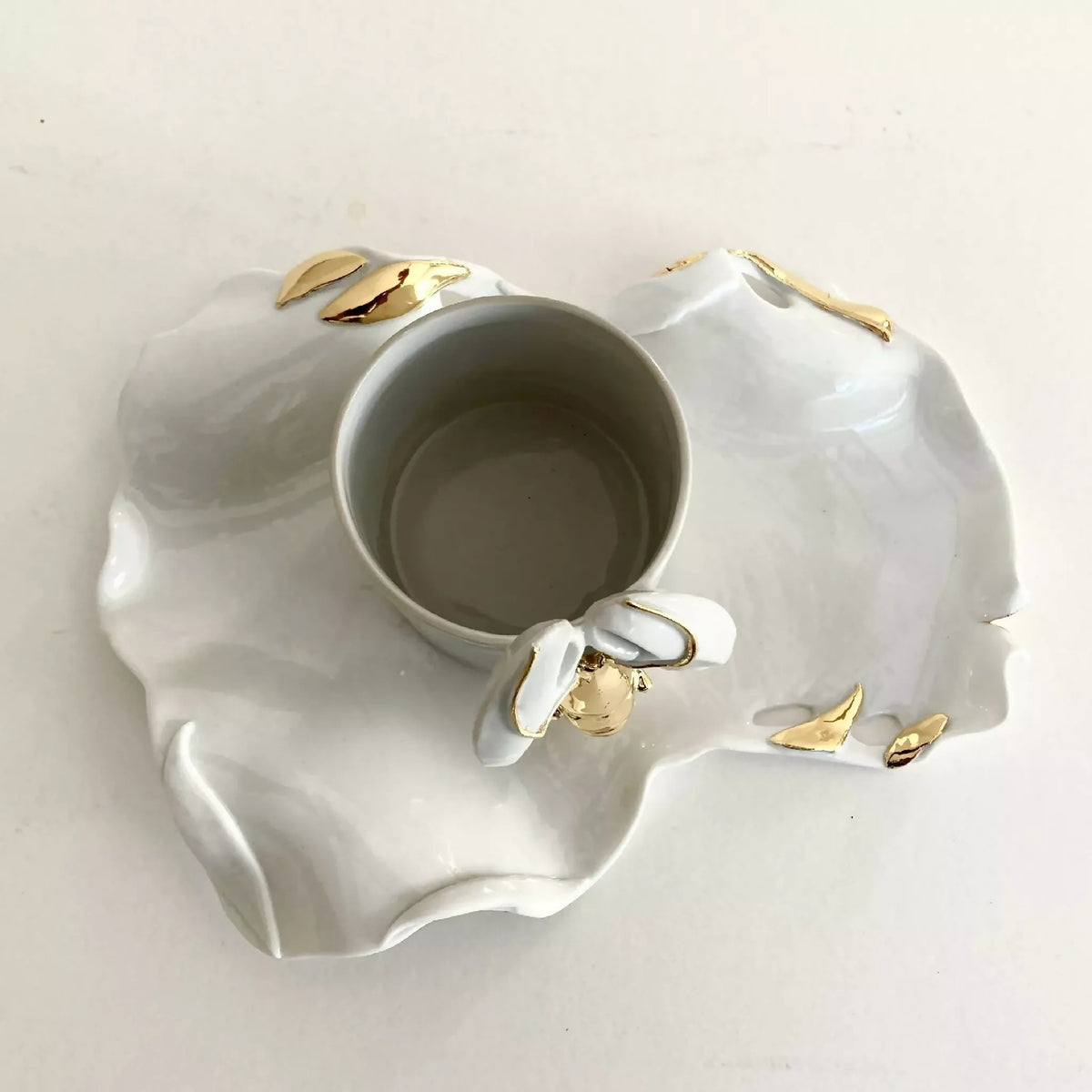 Tasse blanche posée sur soucoupe homard ronde, motif et finitions dorées.