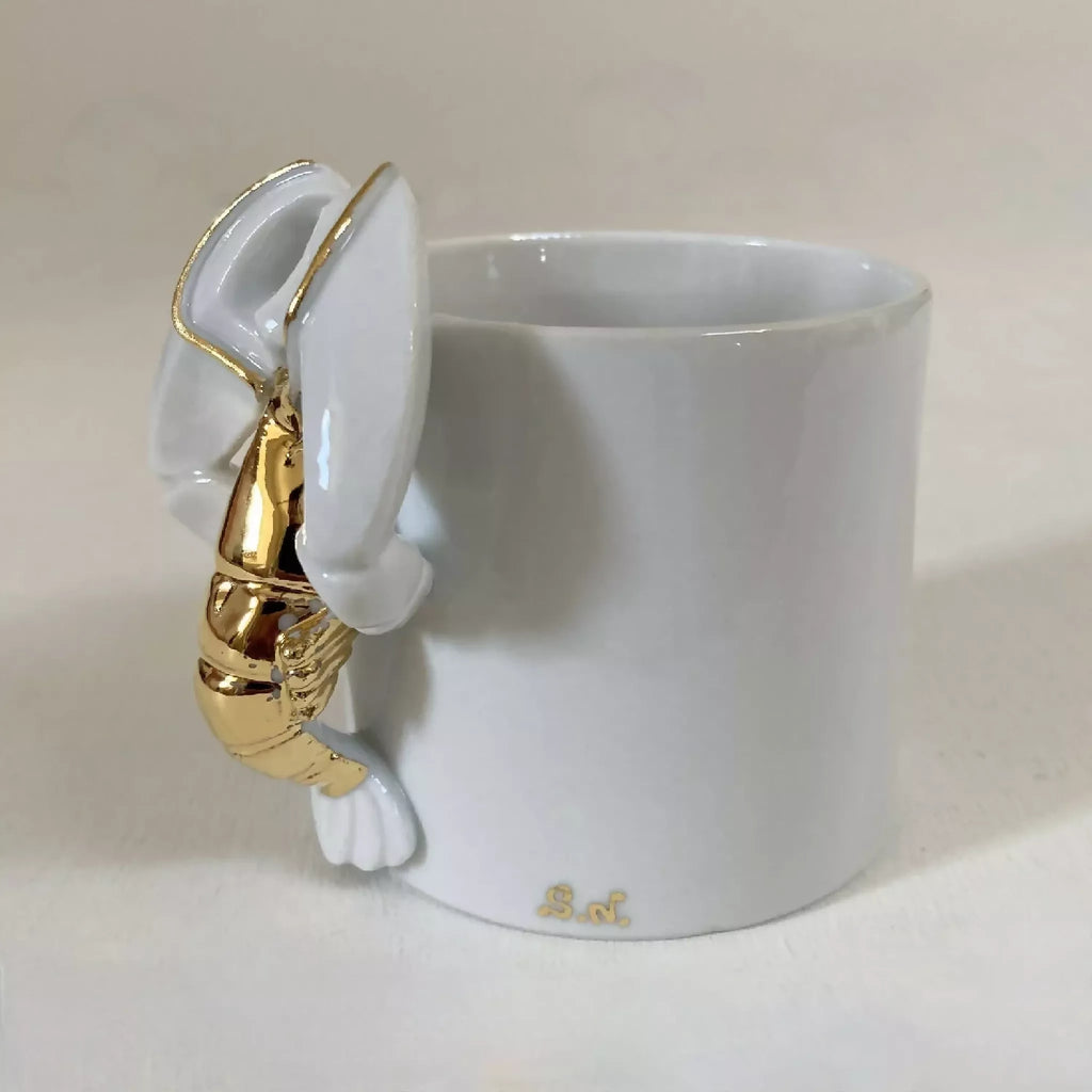 Tasse blanche avec figurine de homard doré accrochée à l’anse