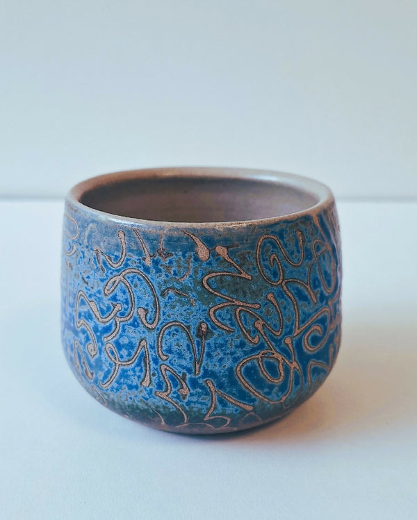 Tasse ronde en céramique bleue avec motifs décoratifs gravés sur le pourtour