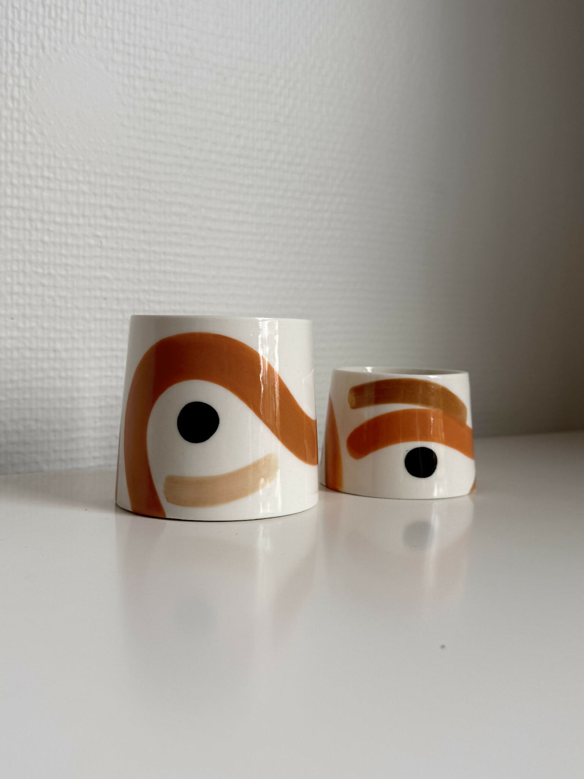 Petites tasses trapèzes blanches à motifs orange et yeux noirs, vue rapprochée.