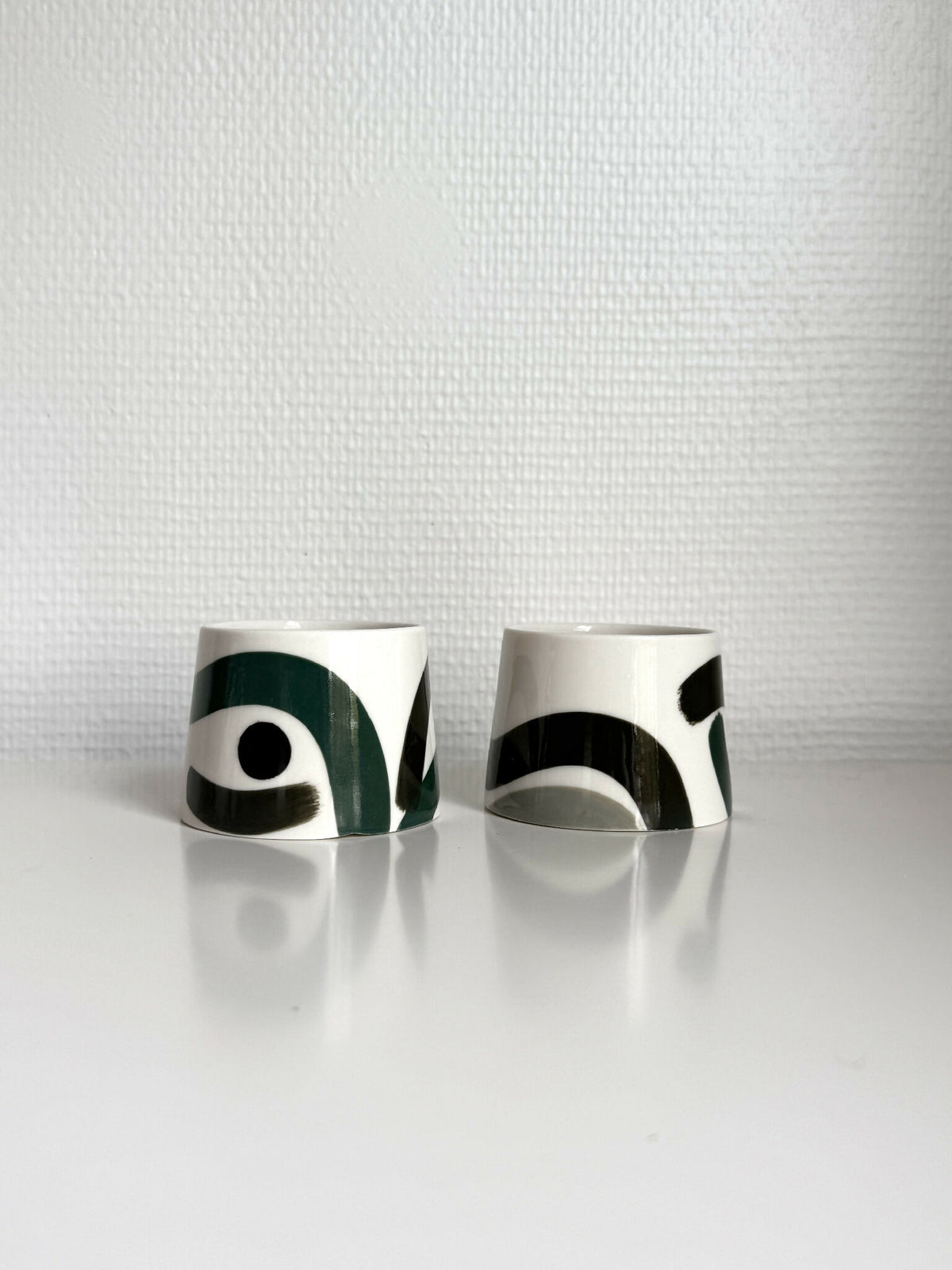 Petites tasses trapèzes blanches à motifs vert foncé et noir, deux exemplaires.