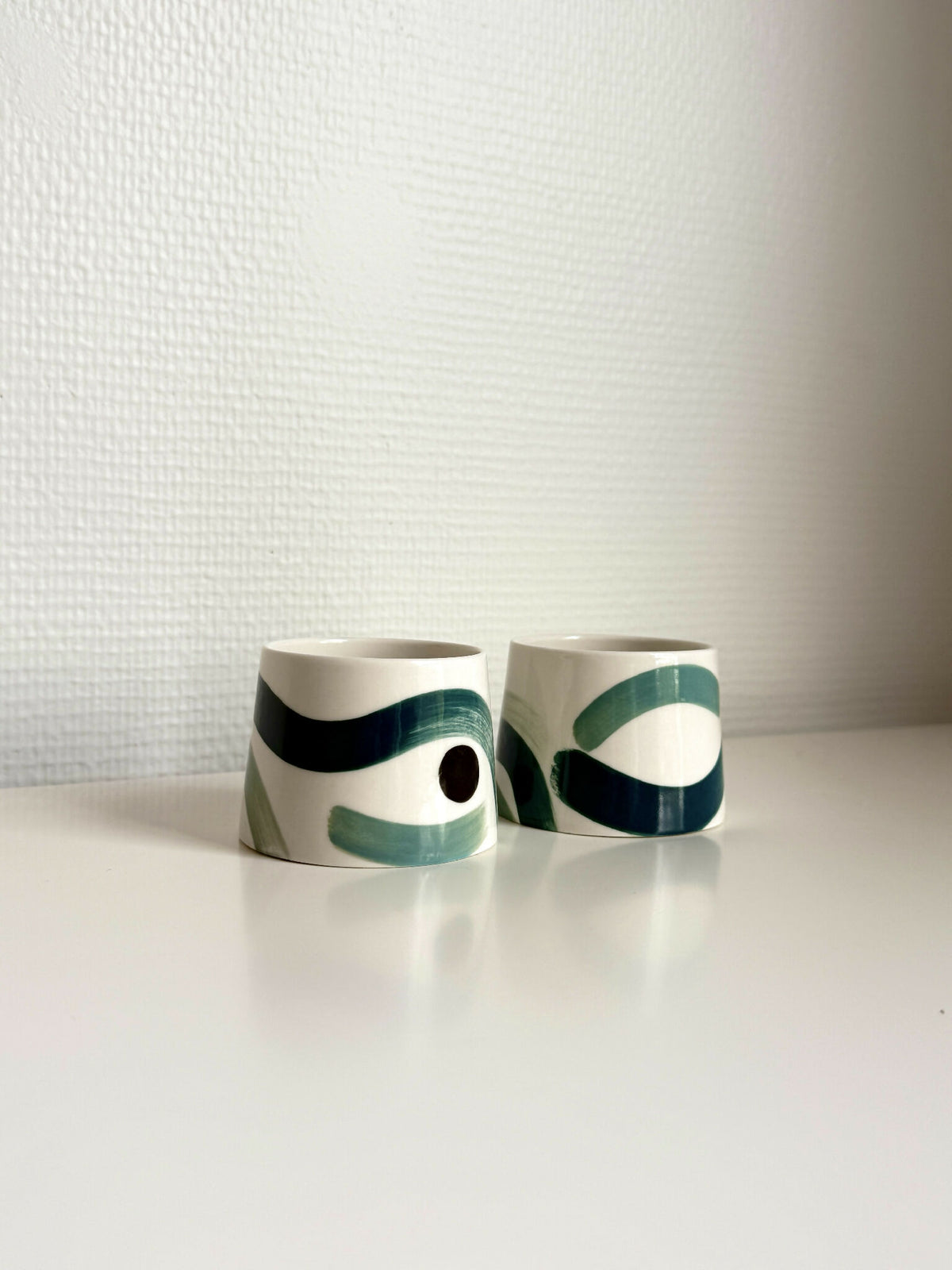Petites tasses trapèzes blanches à motifs vert foncé et noir, deux tasses.