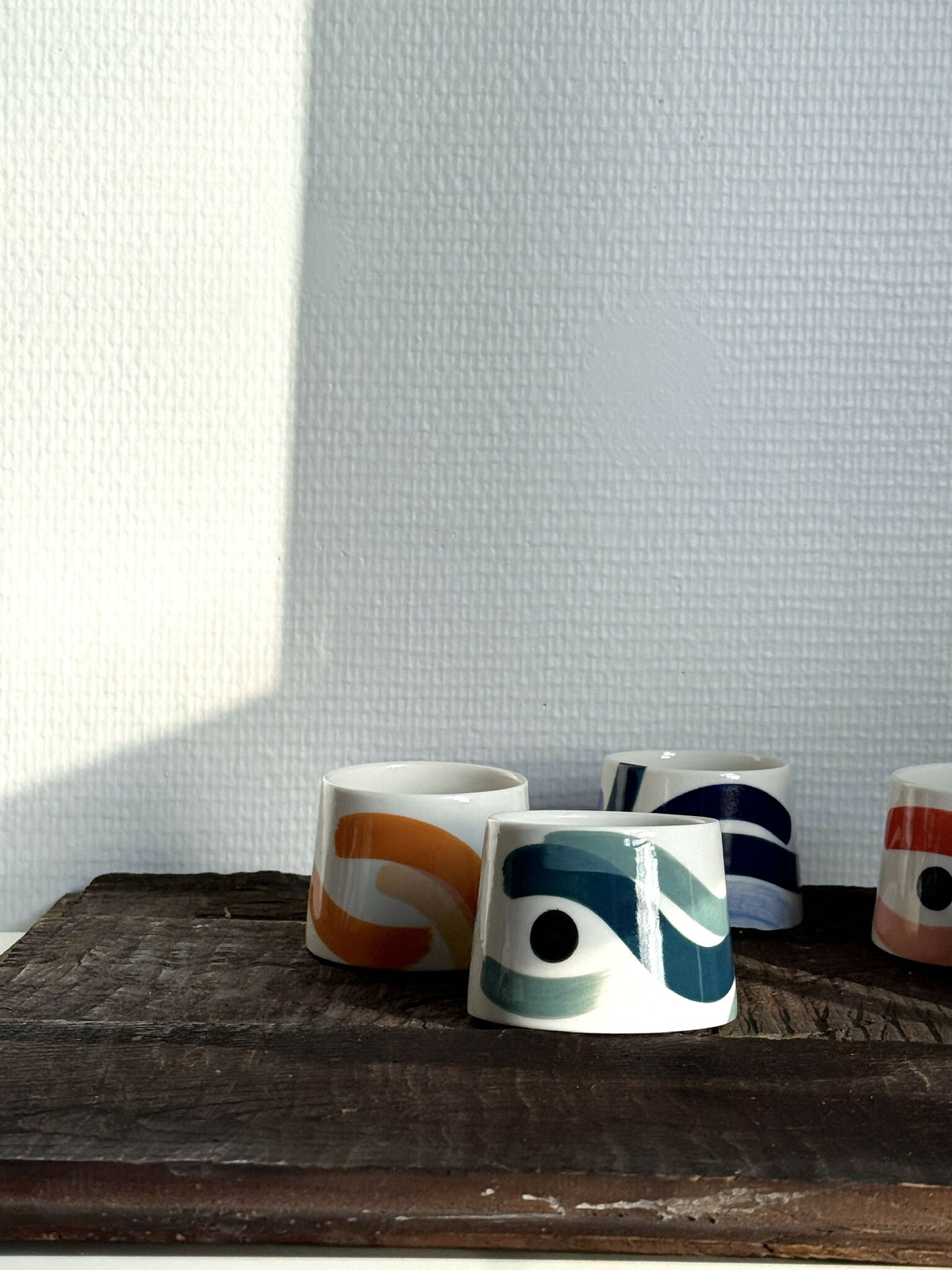 Petites tasses trapèzes blanches à motifs bleus, verts et orange, alignées sur tablette.
