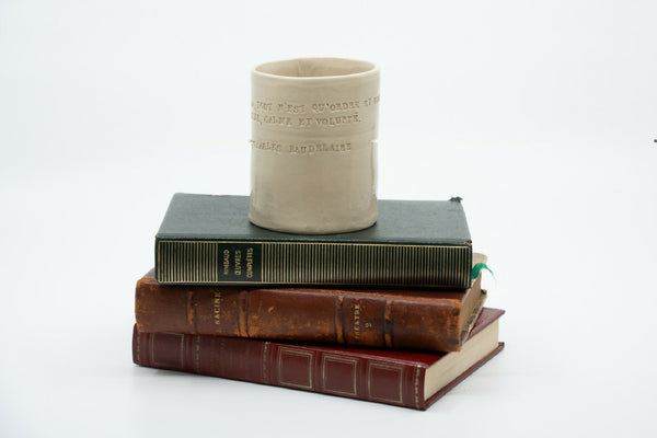 Tasse-poème en céramique beige, posée sur deux livres reliés