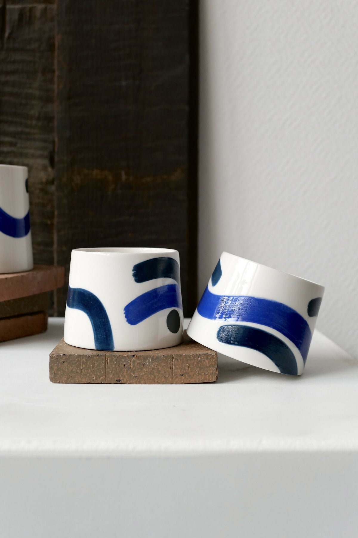 Petites tasses trapèzes blanches à motifs bleus, deux exemplaires sur socle.