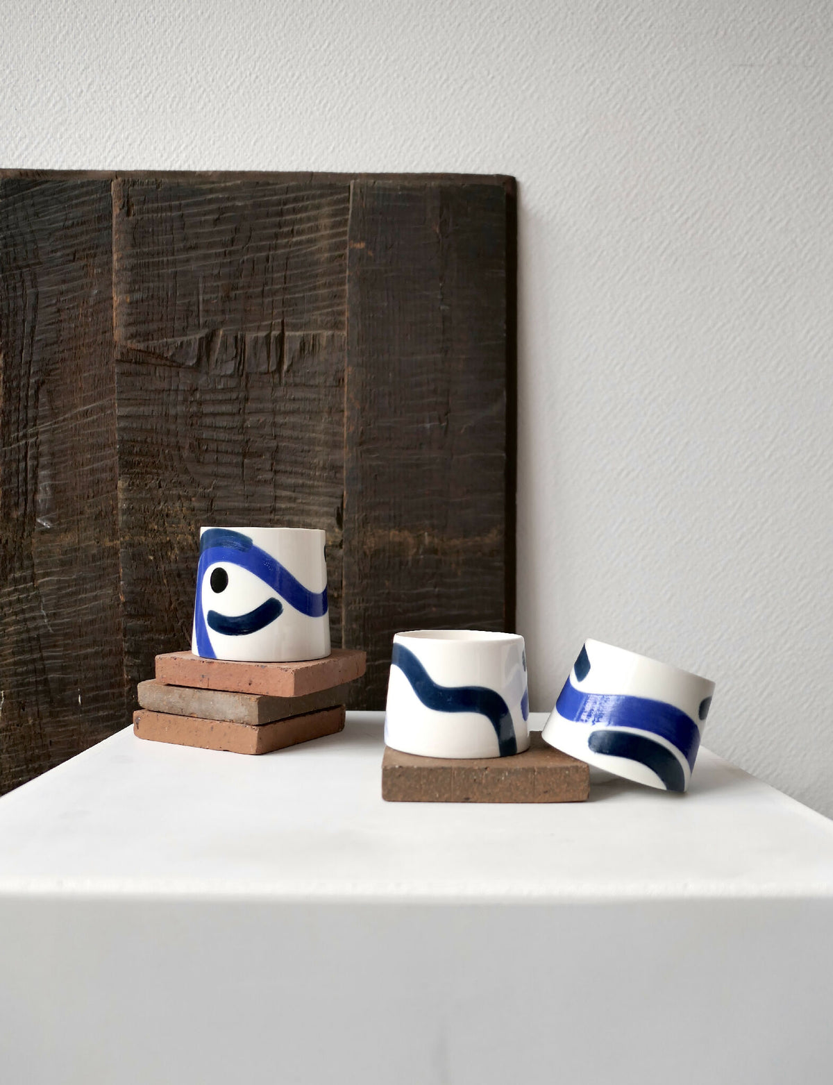 Petite tasse trapèze blanche à motifs bleus, vue en perspective sur socle.