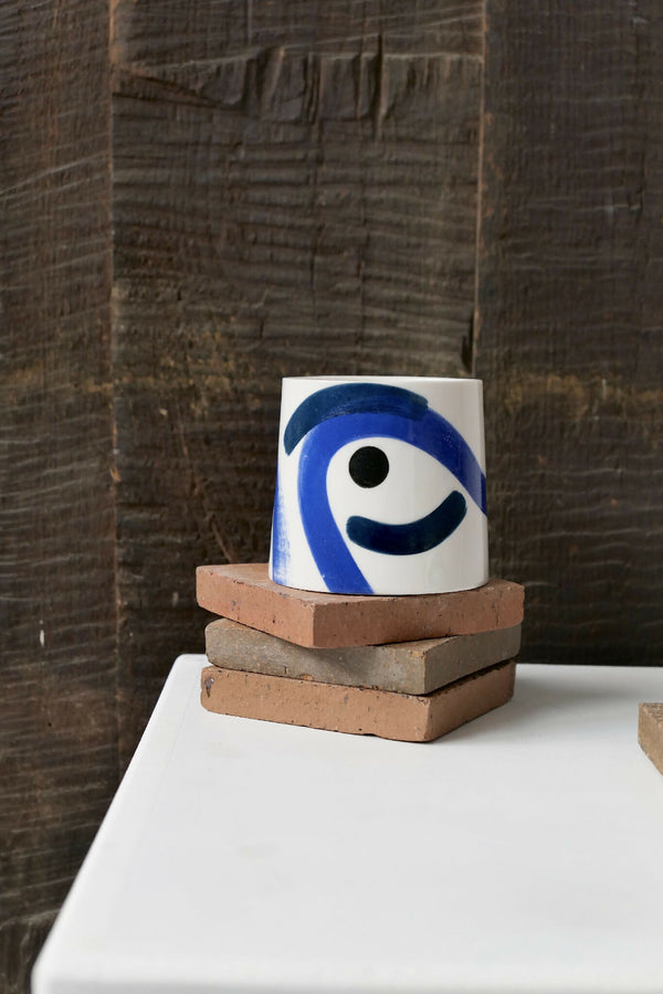 Grande tasse trapèze en céramique blanche à motif bleu, posée sur socle.