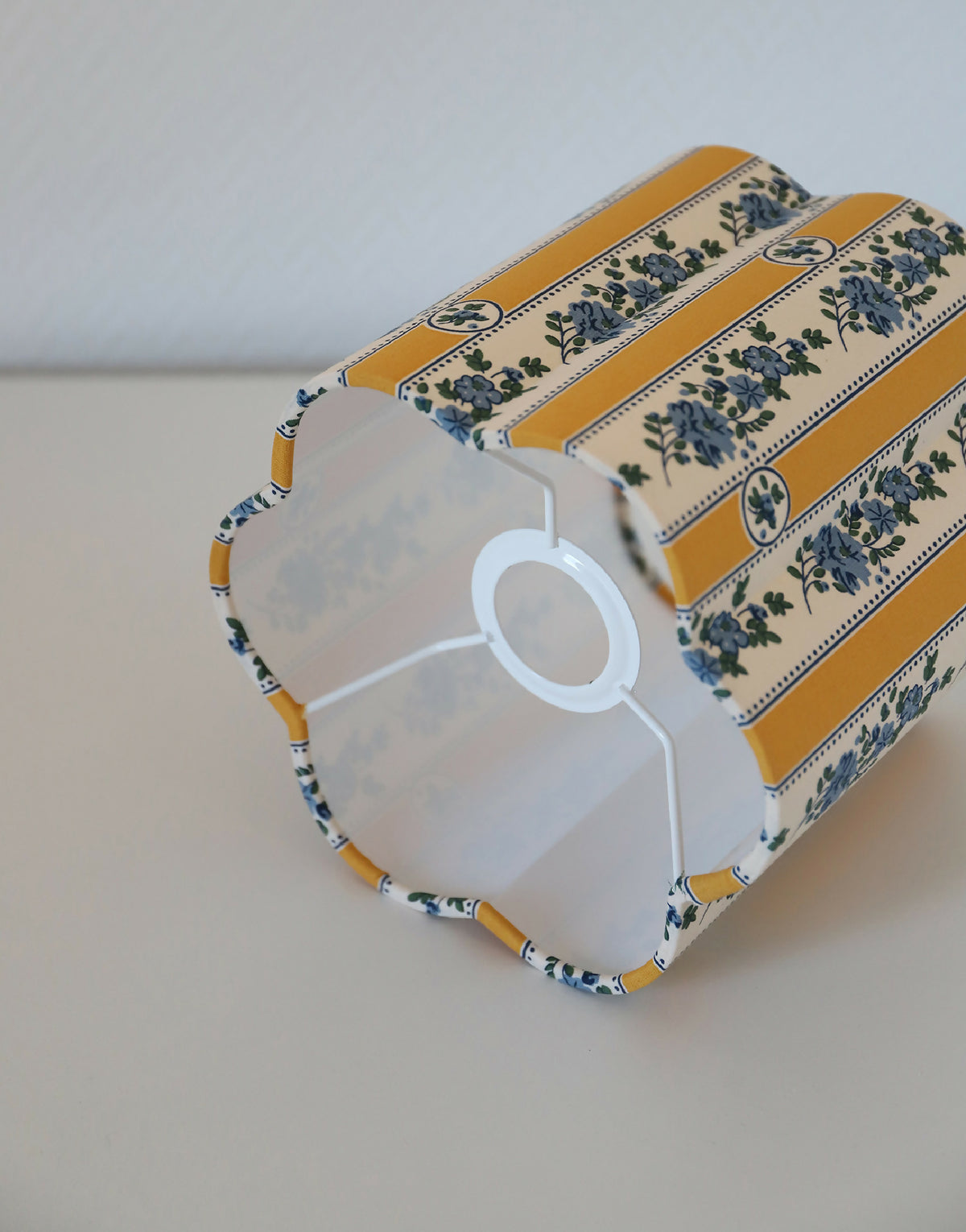 Abat-jour forme fleur en tissu jaune à rayures verticales et motifs bleus.