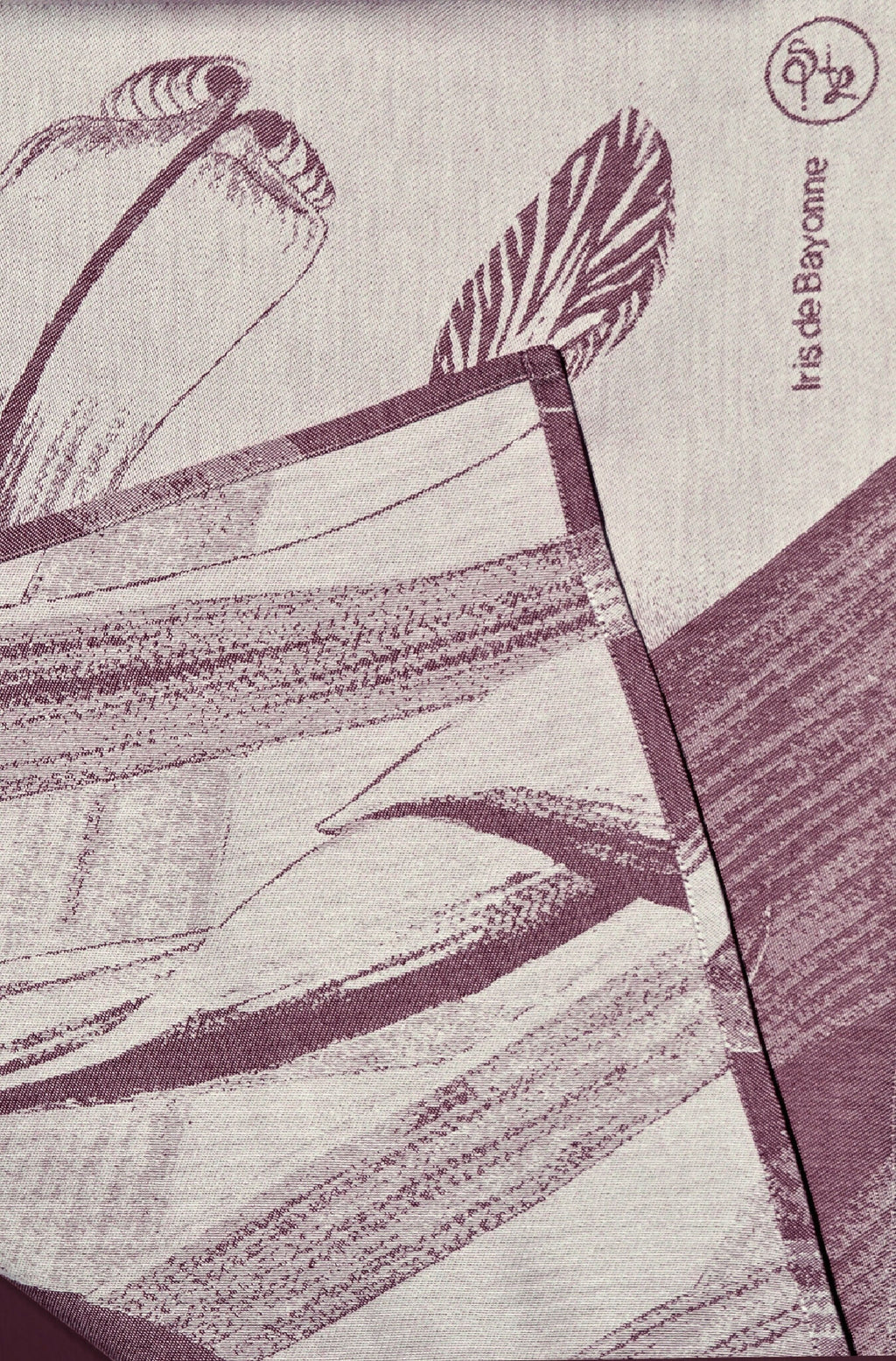 Détail de torchon imprimé : plumes et feuilles violet sur fond clair.